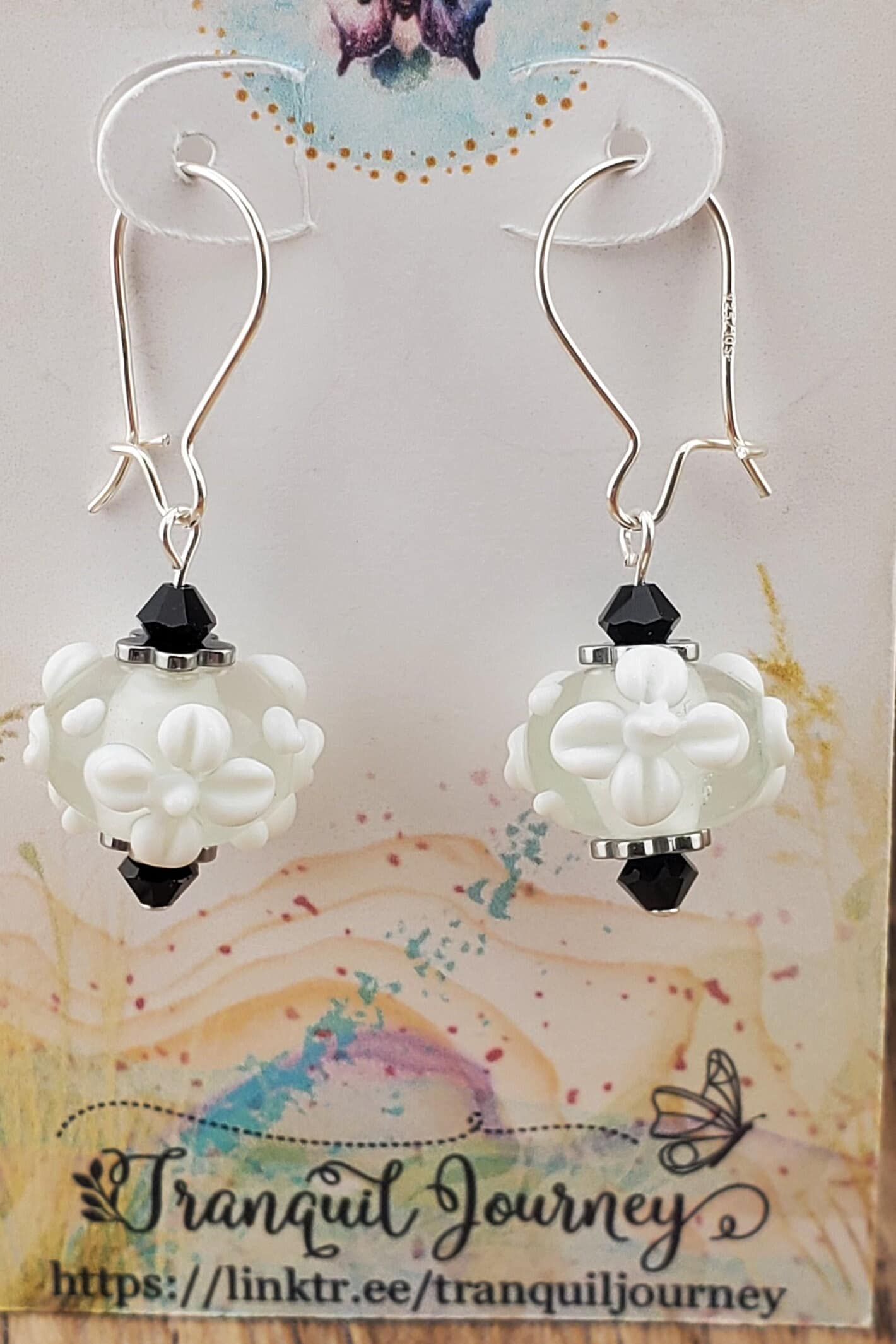 SF Snow Petal Sparkle Artisan Glass Earrings, Lampwork Glass Bead handcrafted by a talented artisan, Silver Filled Earring Wire. White floral lampwork bead accented by black crystals.