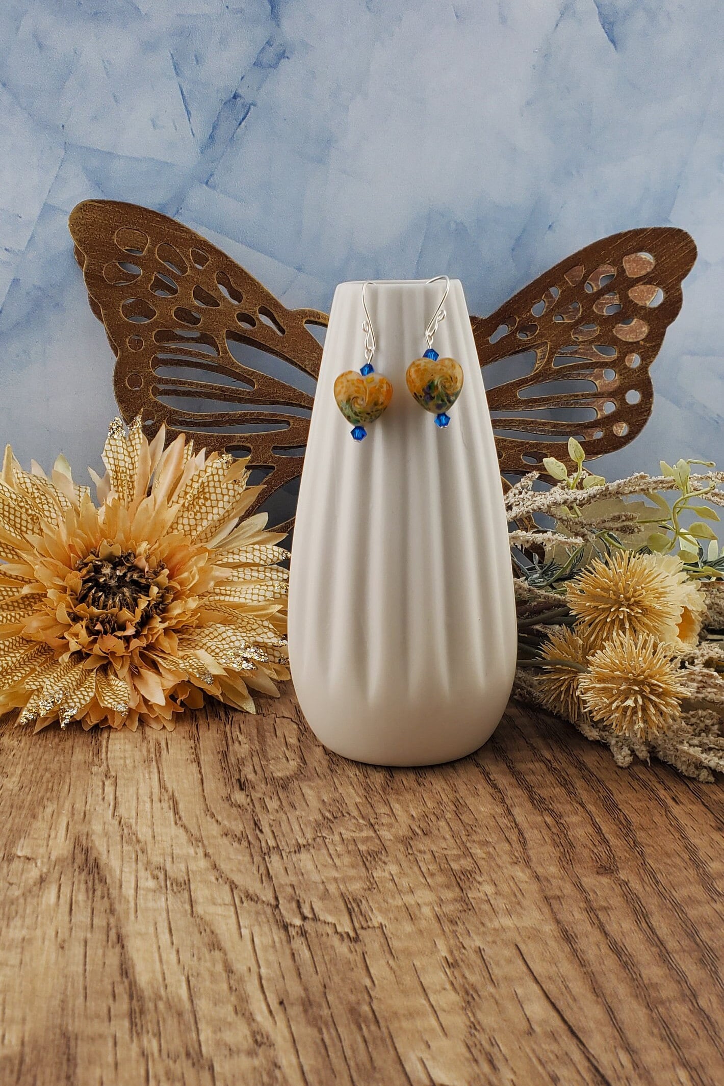 SF Golden Serenade Heart Artisan Glass Earrings, Lampwork Glass Bead handcrafted by a talented artisan, Silver Filled Earring Wire. Golden heart lampwork bead with blue and green swirls. Blue crystal beads accent the heart.