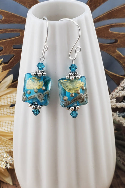 SF Golden Horizon Blues Artisan Glass Earrings, Lampwork Glass Bead handcrafted by a talented artisan, Silver Filled Earring Wire. Teal and golden colors fill this lampwork bead and it is accented with teal crystals.