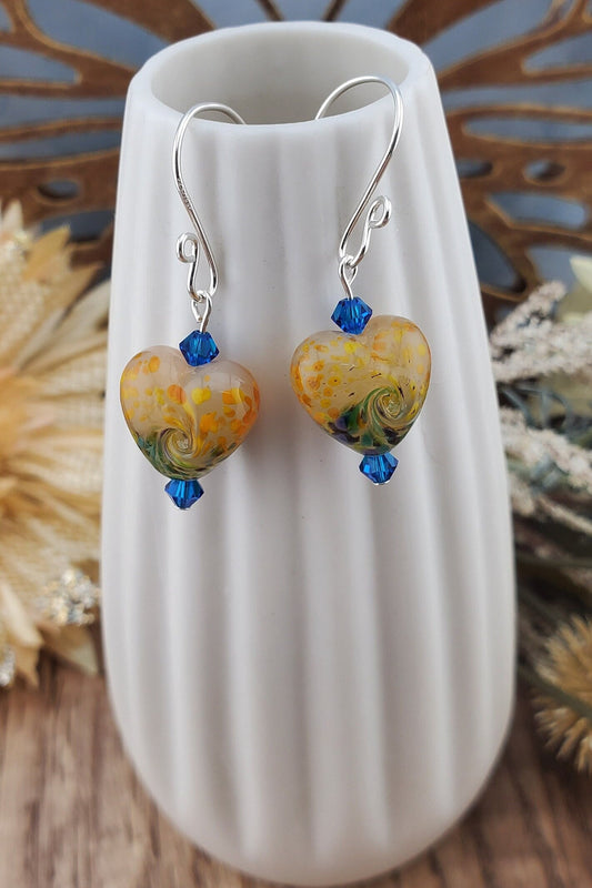 SF Golden Serenade Heart Artisan Glass Earrings, Lampwork Glass Bead handcrafted by a talented artisan, Silver Filled Earring Wire. Golden heart lampwork bead with blue and green swirls. Blue crystal beads accent the heart.