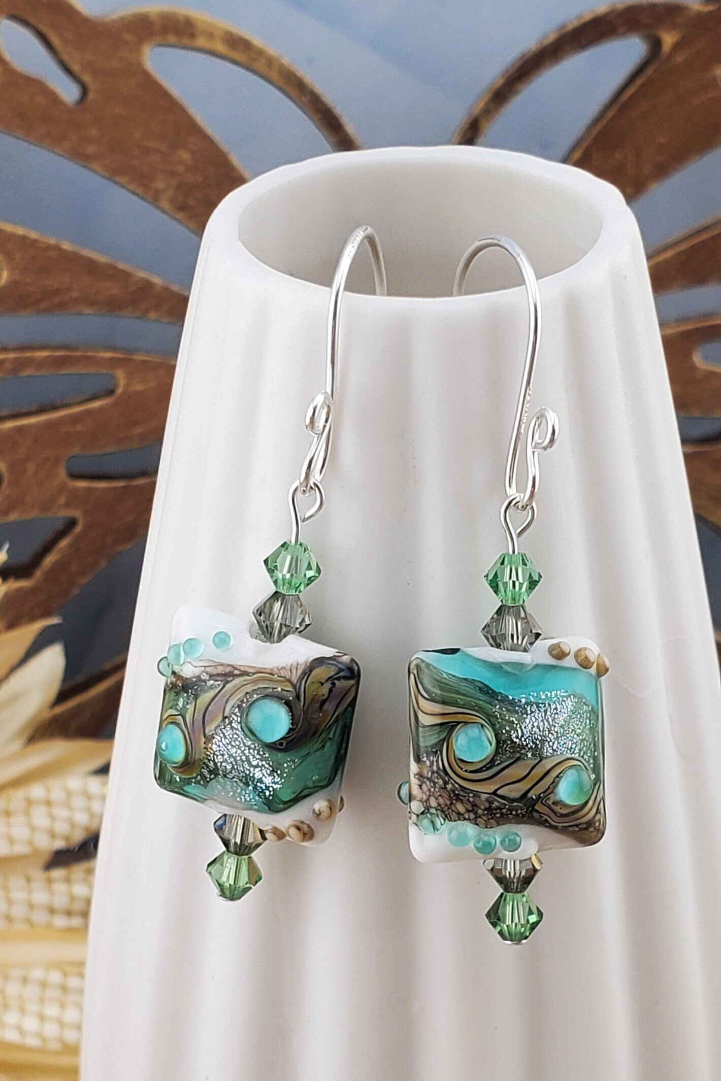 SF Coastal Breeze Artisan Glass Earrings, Lampwork Glass Bead handcrafted by a talented artisan, Silver Filled Earring Wire. Shades of blue, green and browns compliment this lampwork bead. Green and brown crystals adorn the bead.