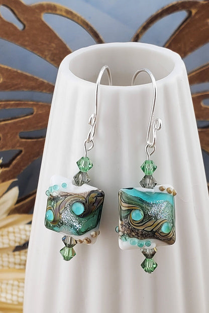 SF Coastal Breeze Artisan Glass Earrings, Lampwork Glass Bead handcrafted by a talented artisan, Silver Filled Earring Wire. Shades of blue, green and browns compliment this lampwork bead. Green and brown crystals adorn the bead.