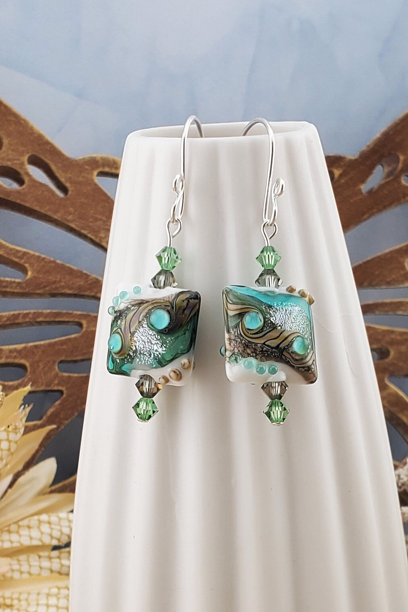 SF Coastal Breeze Artisan Glass Earrings, Lampwork Glass Bead handcrafted by a talented artisan, Silver Filled Earring Wire. Shades of blue, green and browns compliment this lampwork bead. Green and brown crystals adorn the bead.