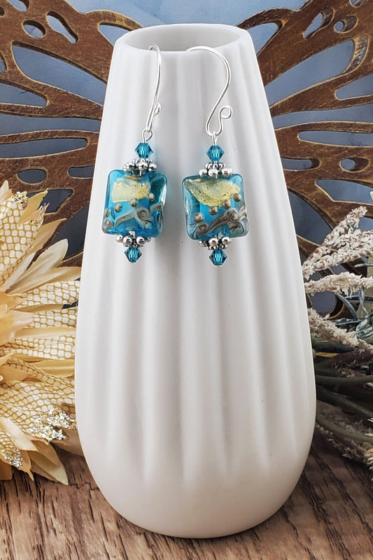 SF Golden Horizon Blues Artisan Glass Earrings, Lampwork Glass Bead handcrafted by a talented artisan, Silver Filled Earring Wire. Teal and golden colors fill this lampwork bead and it is accented with teal crystals.